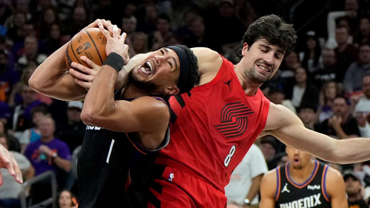 Phoenix Suns guard Devin Booker (1) gets fouled by Portland Trail Blazers forward Deni Avdija (8) during the second half of an NBA play-in tournament basketball game, Tuesday, April 14, 2026, in Phoenix.