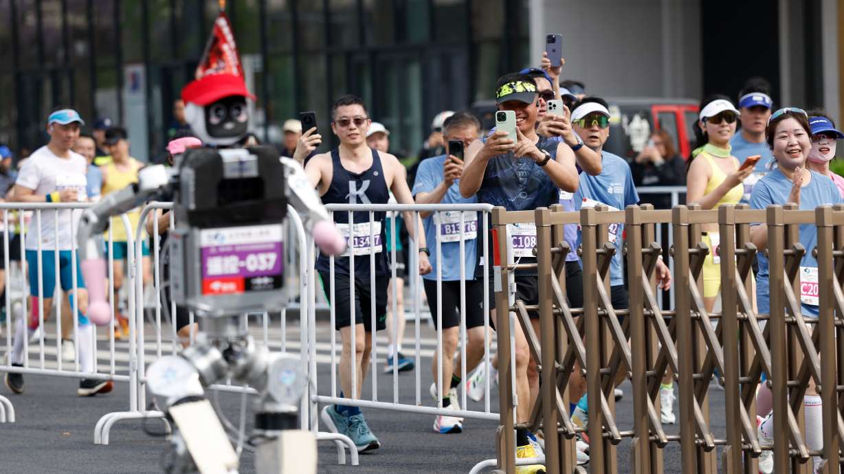 Runners take pictures of a humanoid robot in the second Beijing E-Town Half Marathon and Humanoid Robot Half Marathon in Beijing Sunday, April 19, 2026.