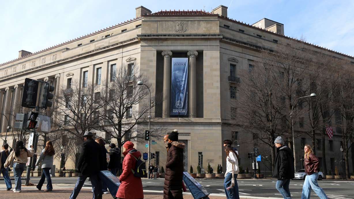 Tourists walk past a banner with President Donald Trump hanging on the Department of Justice, Feb. 27, in Washington.