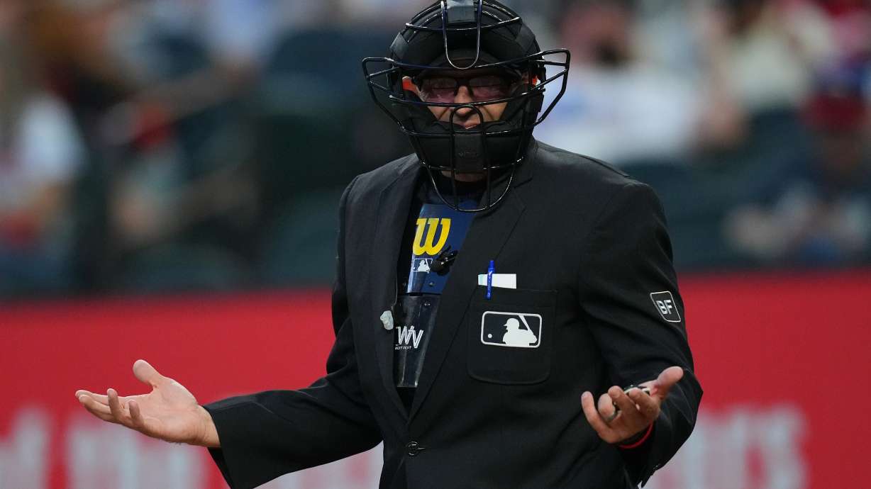 Home plate umpire Alex MacKay reacts toward the Seattle Mariners bench after calling a strike during the third inning of a baseball game against the Texas Rangers, Monday, April 6, 2026, in Arlington, Texas.