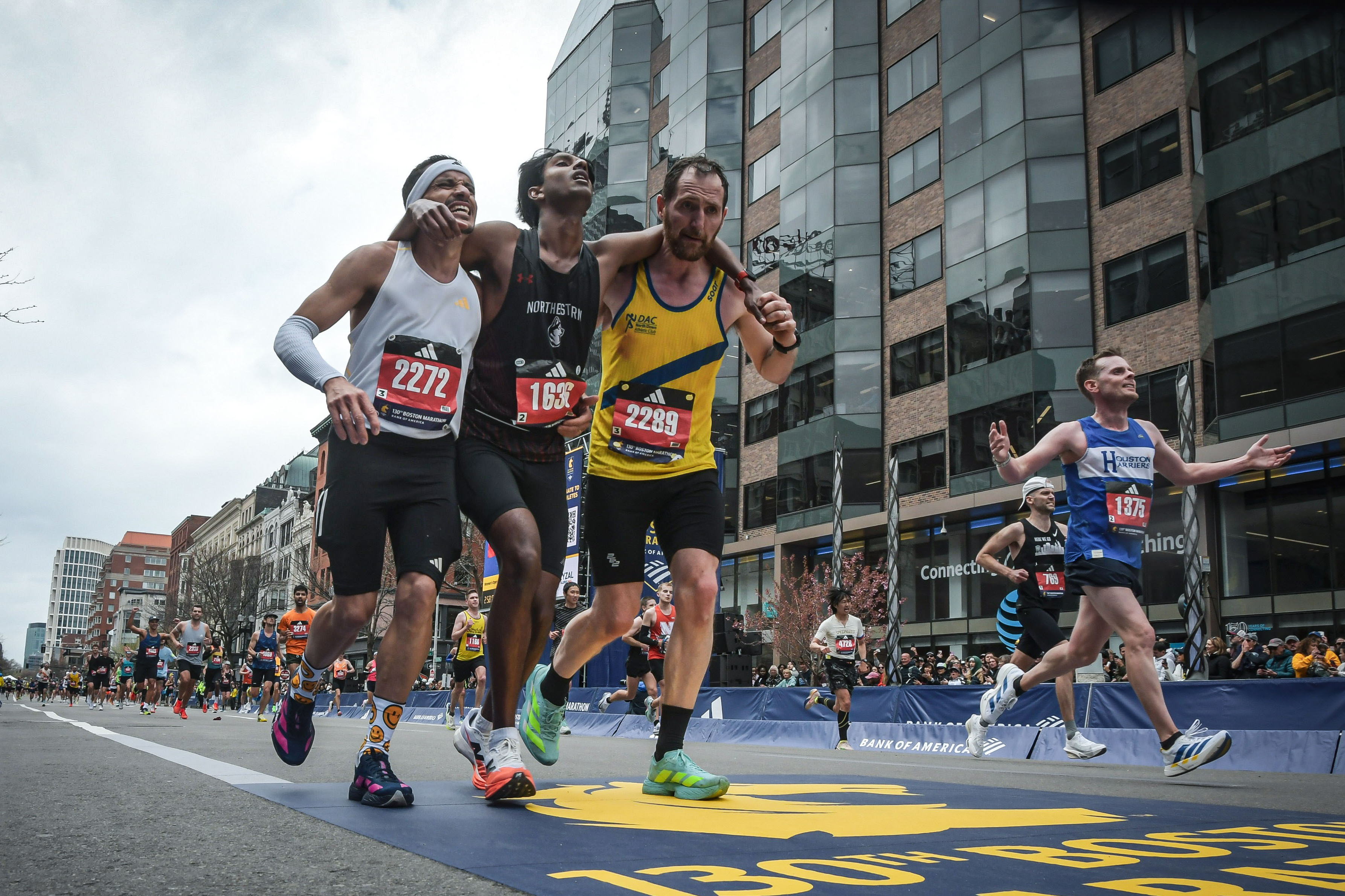 This photo provided by the Boston Athletic Association and Marathonfoto shows Boston Marathon runners Robson De Oliveira of Brazil, left, and Aaron Beggs, of Britain, right, helping runner Ajay Haridasse and helped him across the finish line Monday, April 20, 2026, in Boston. 