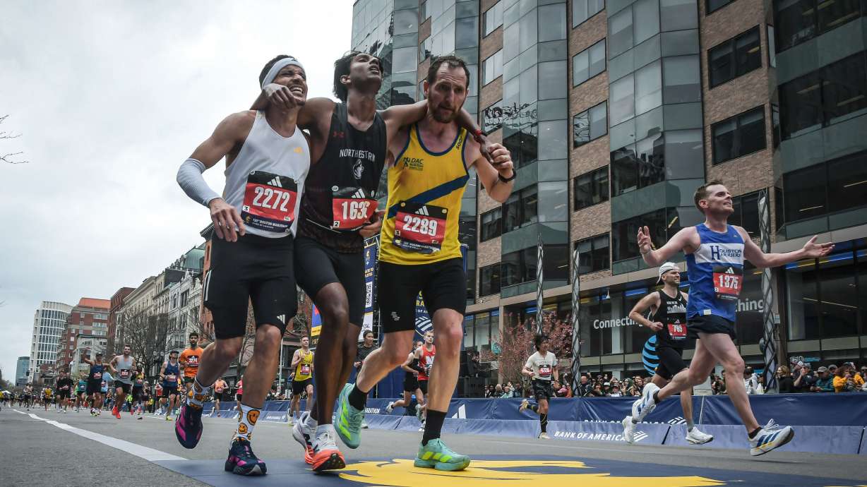 This photo provided by the Boston Athletic Association and Marathonfoto shows Boston Marathon runners Robson De Oliveira of Brazil, left, and Aaron Beggs, of Britain, right, helping runner Ajay Haridasse and helped him across the finish line Monday in Boston.