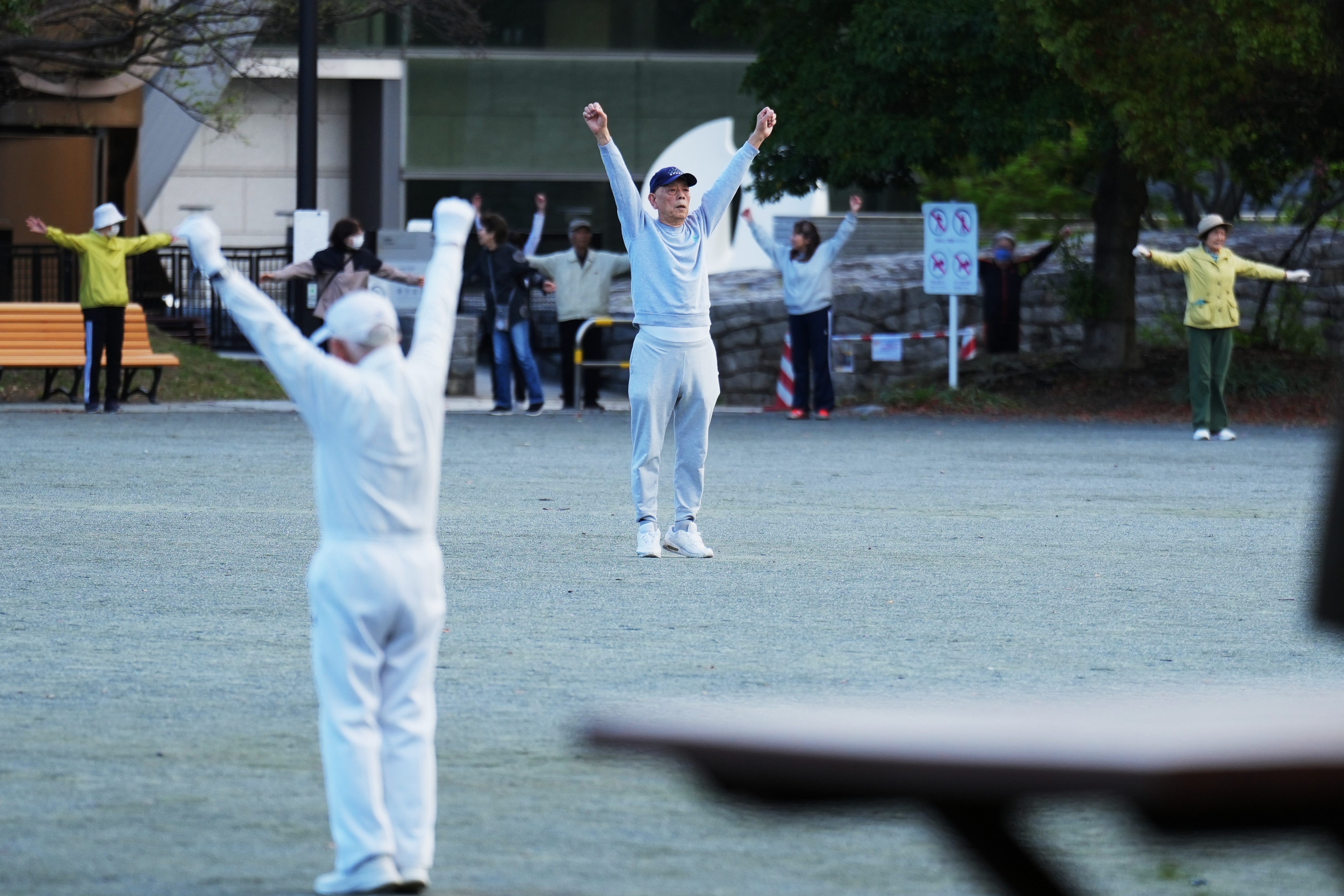 People perform a stretching exercise while listening to music and guidance from radio at a public park in Tokyo, Monday, April 6, 2026. 