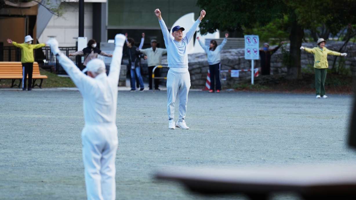 People perform a stretching exercise while listening to music and guidance from radio at a public park in Tokyo, Monday, April 6, 2026.