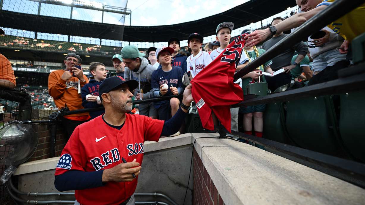 Boston Red Sox manager Alex Cora, foreground, gives autographs to fans before a baseball game against the Baltimore Orioles, Friday, April 24, 2026, in Baltimore.