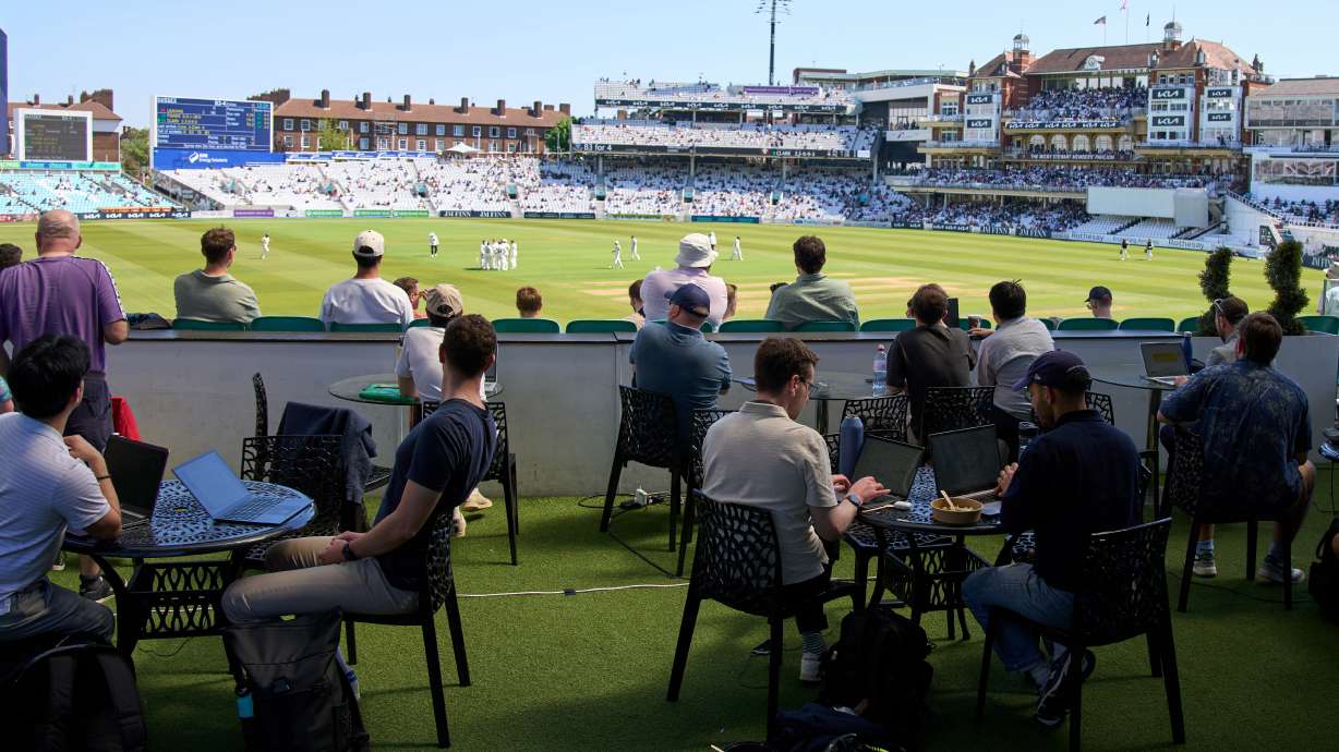 People work and watch cricket during a Surrey against Sussex County Championship cricket match at the Kia Oval in London, Friday, May 1, 2026.
