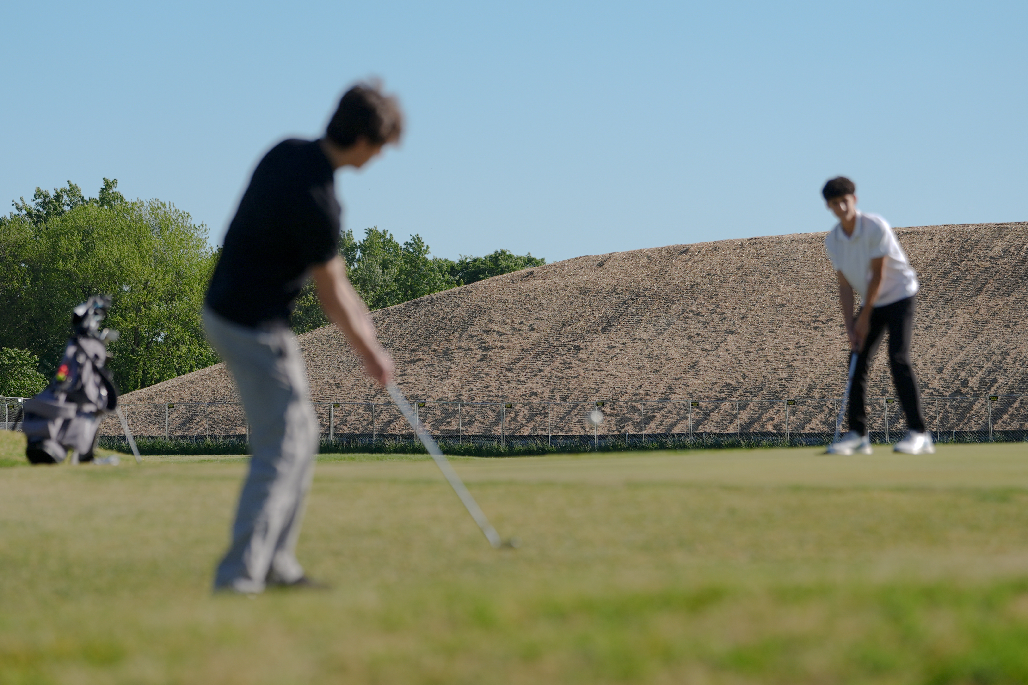 A pile of debris is seen in the background as Roman Sandoli, right, prepares to putt at the East Potomac Golf Course, Sunday, May 3, 2026, in Washington. 