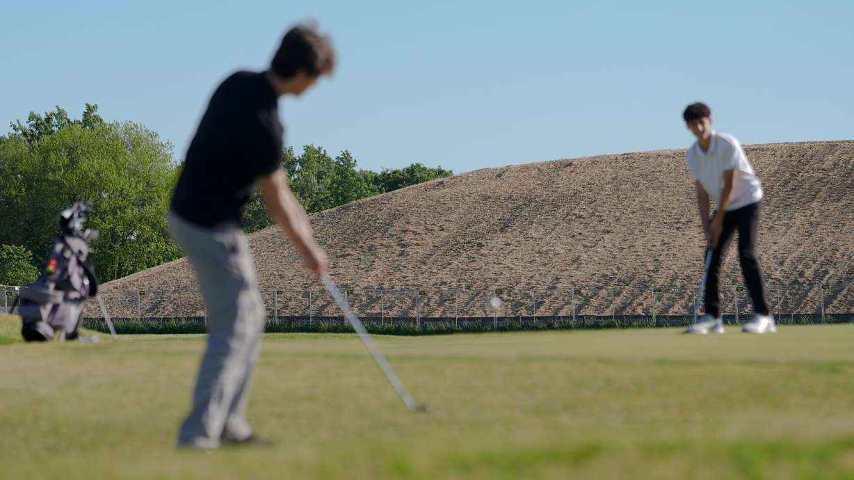 A pile of debris is seen in the background as Roman Sandoli, right, prepares to putt at the East Potomac Golf Course, Sunday, May 3, 2026, in Washington.