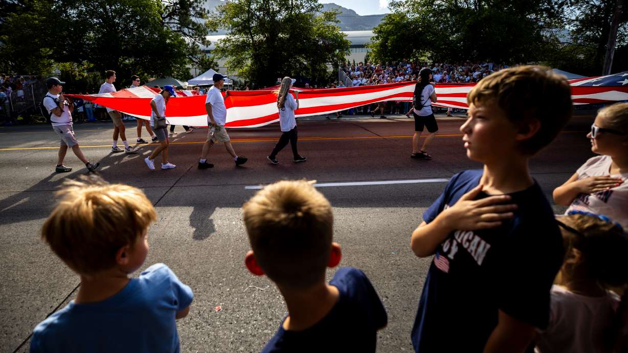 Brigham Holmstrom, 10, right, places his hand on his heart as the American flag is carried in the Freedom Festival Parade in Provo on July 4, 2025.