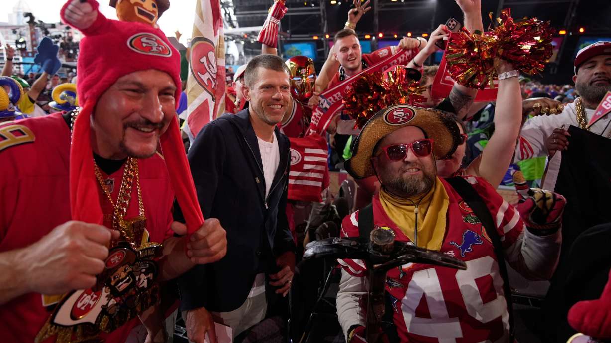 Former NFL player Andy Lee, center, poses with San Francisco 49ers fans during the second round of the NFL football draft, Friday, April 24, 2026, in Pittsburgh.