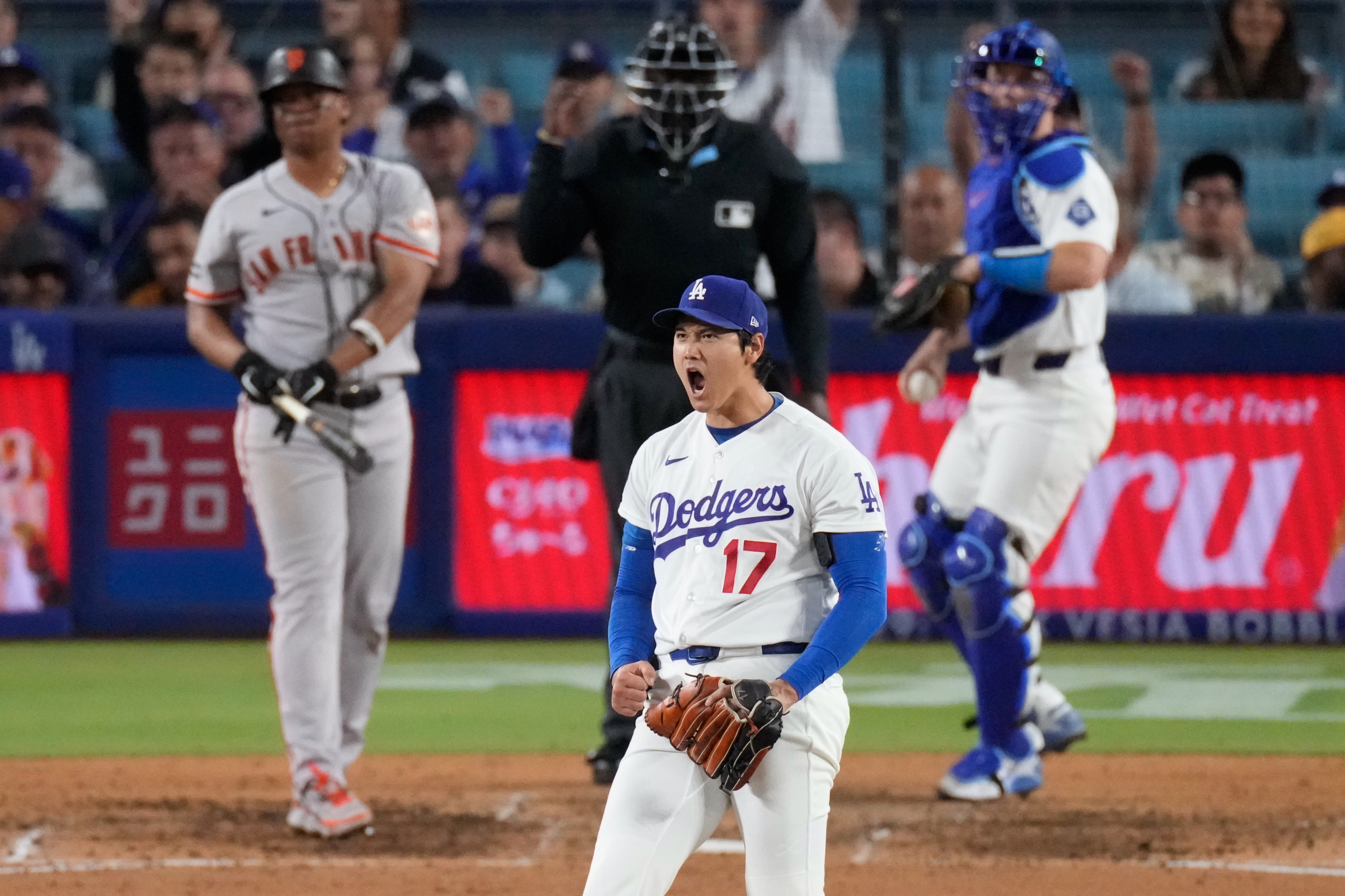 Los Angeles Dodgers two-way player Shohei Ohtani, center, reacts after striking out San Francisco Giants' Rafael Devers, left, as catcher Will Smith gets ready to throw the ball back during the sixth inning of a baseball game Wednesday, May 13, 2026, in Los Angeles. 