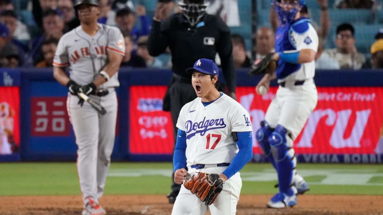 Los Angeles Dodgers two-way player Shohei Ohtani, center, reacts after striking out San Francisco Giants' Rafael Devers, left, as catcher Will Smith gets ready to throw the ball back during the sixth inning of a baseball game Wednesday, May 13, 2026, in Los Angeles.