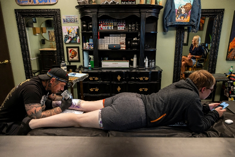 Randolph Torres tattoos the leg of Lexys Siebrands as her mother Jyl Siebrands watches in Fort Morgan, Colorado, May 11.