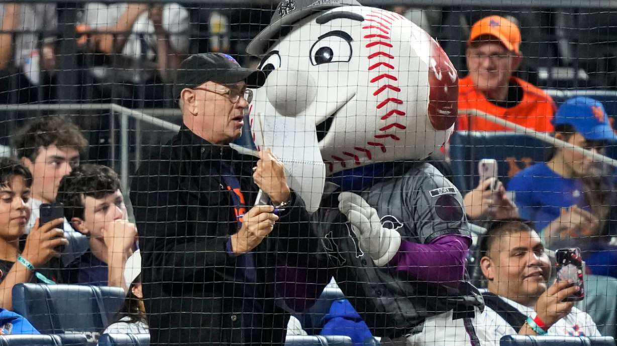 Actor/filmmaker Tom Hanks, center left, stands with Mr. Met, center right, during the sixth inning of a baseball game between the New York Mets and the New York Yankees, Saturday, May 16, 2026, in New York.