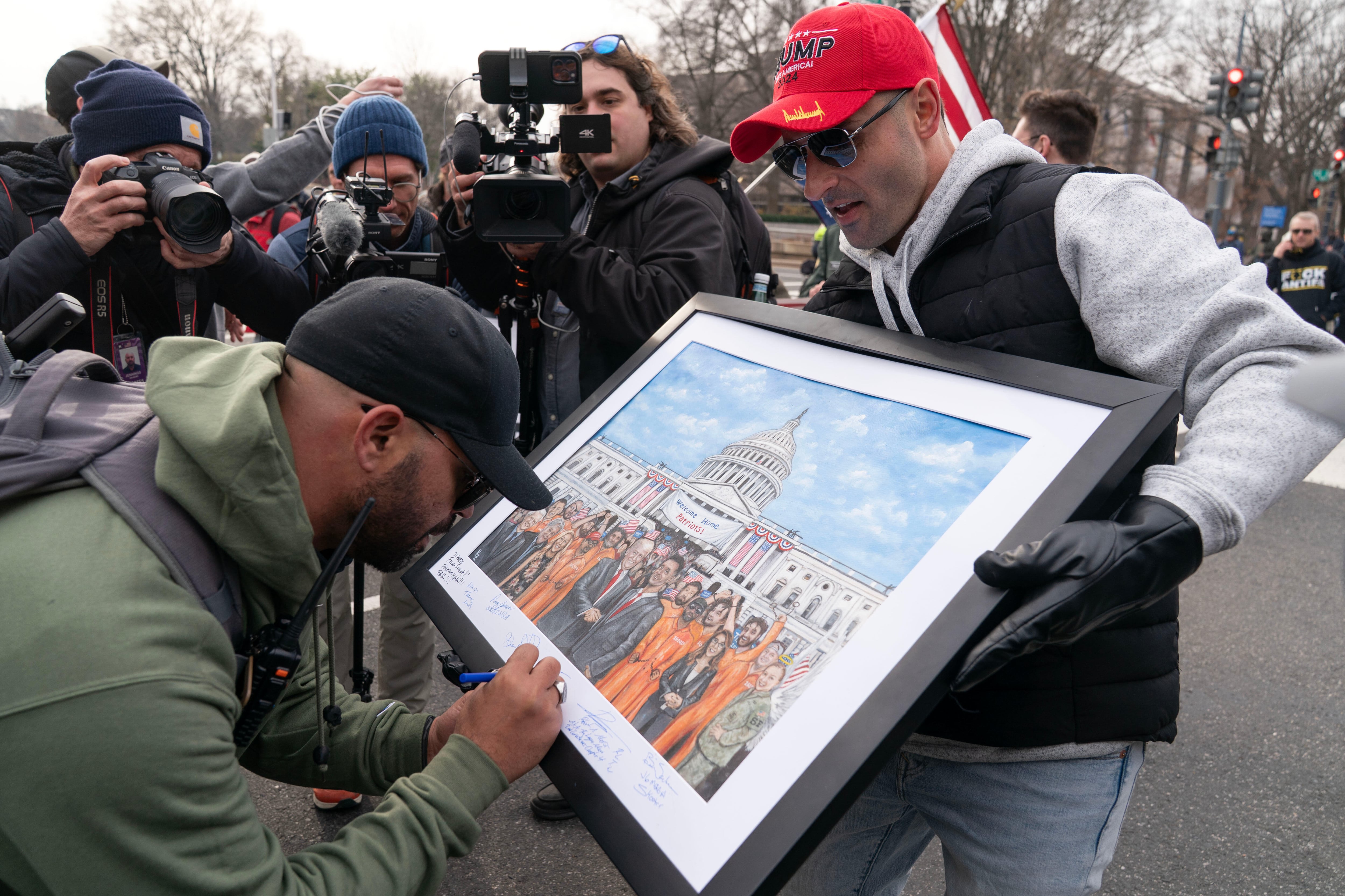 Enrique Tarrio, left, the former head of the Proud Boys, signs a painting as demonstrators march on Constitution Avenue during the Jan. 6 Anniversary, Jan. 6, 2026, in Washington.