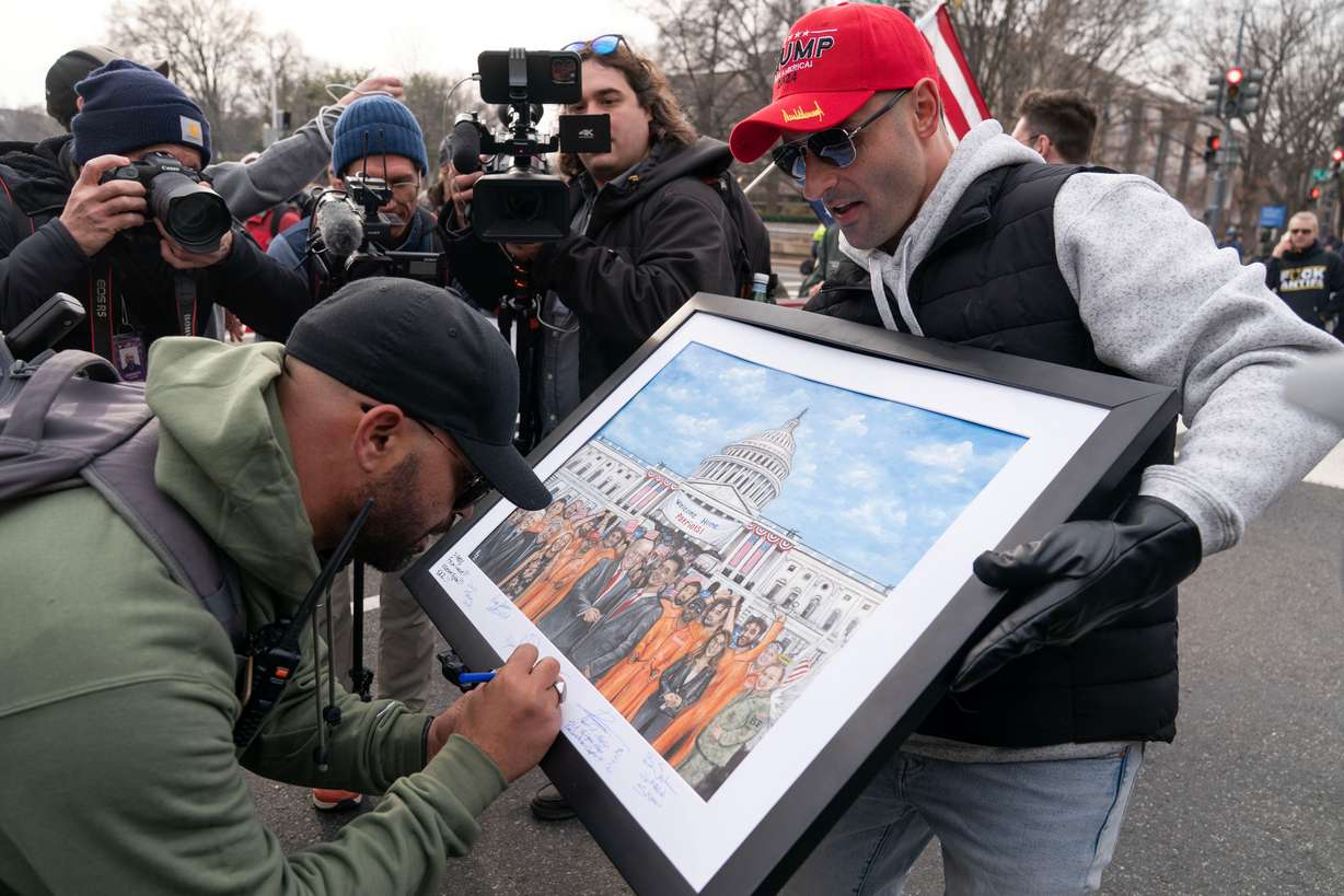 Enrique Tarrio, left, the former head of the Proud Boys, signs a painting as demonstrators march on Constitution Avenue during the Jan. 6 Anniversary, Jan. 6, 2026, in Washington.