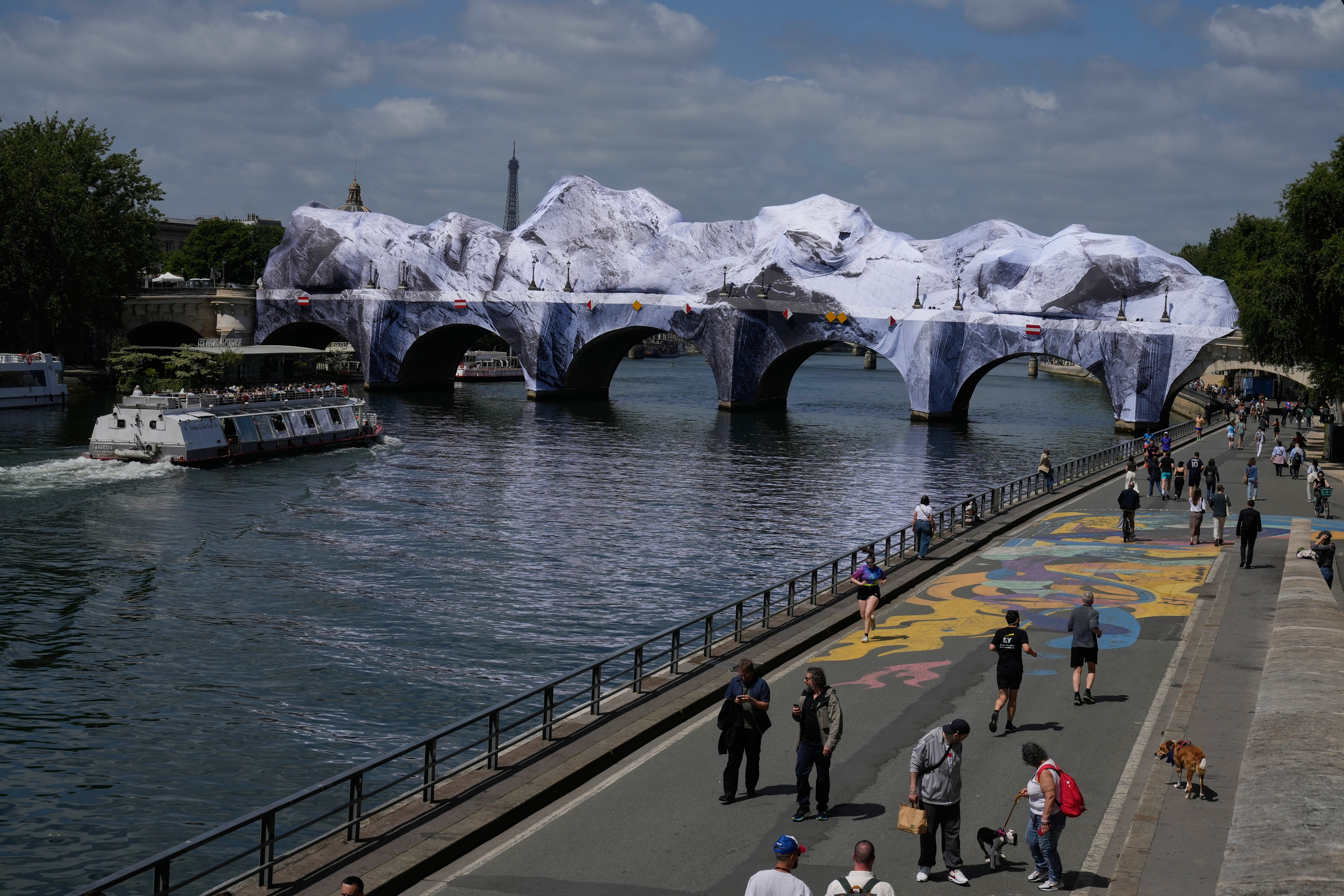 People walk along the Seine river next to "The Pont Neuf Cave," an inflated art installation by French street artist JR, on Paris' oldest bridge, the Pont Neuf, Thursday, which will be open to the public from June 6 to June 28. The art was inflated overnight due to recent bad weather.