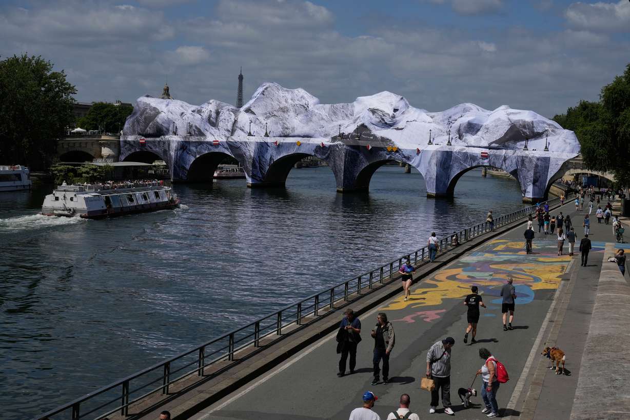People walk along the Seine river next to "The Pont Neuf Cave," an inflated art installation by French street artist JR, on Paris' oldest bridge, the Pont Neuf, Thursday, which will be open to the public from June 6 to June 28. The art was inflated overnight due to recent bad weather.