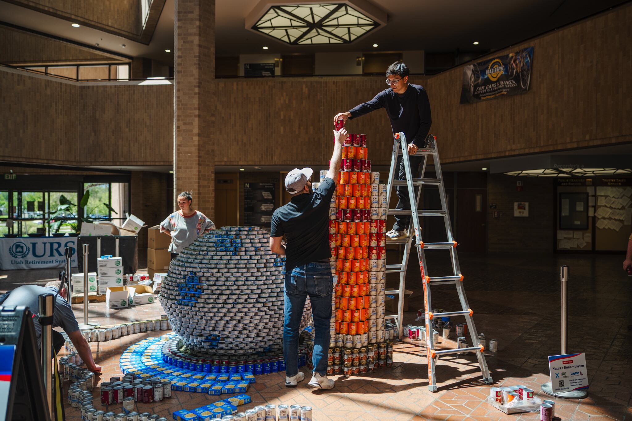 People put together a sculpture made from canned food at the Salt Lake County Government Center in Salt Lake City as part of the America250 celebrations. Various displays can be seen at the county’s different public buildings.