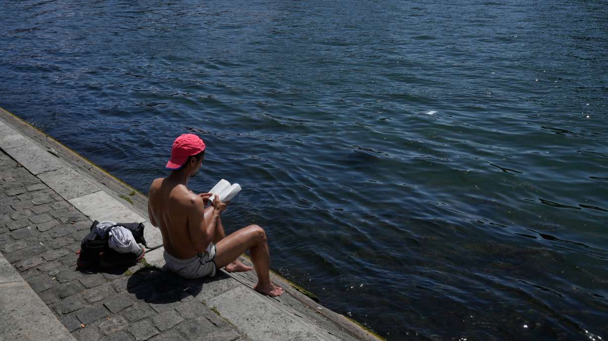 A man reads a book while sitting in the sun along the Seine River in Paris, Monday, May 25, 2026.