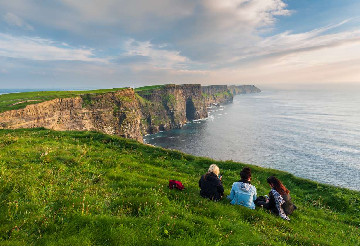 Girls sitting near the edge of the cliffs of Moher in Ireland.