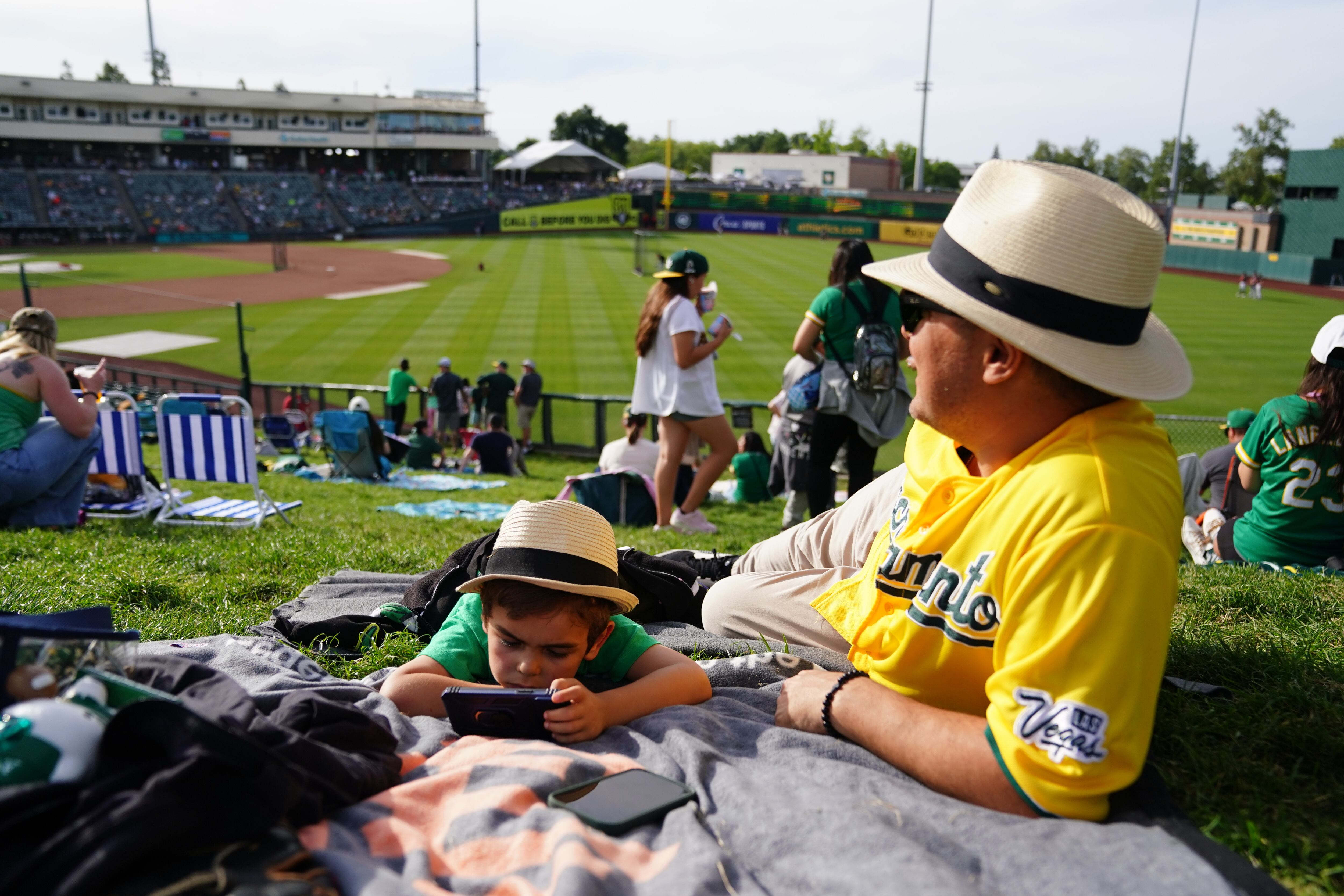 Chris Haley, 6, and his father Chris Haley, of Citrus Heights, Calif., hang out on the lawn area before a baseball game between the Athletics and the Cleveland Guardians, May 1, in West Sacramento, Calif. Sacramento announced on Thursday its own push for an MLB team.