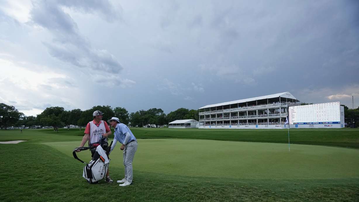 Joel Dahmen, right, reaches into his bag with caddie Jon Reehoorn on the 18th green after play was suspended due to weather during the first round of the Charles Schwab Challenge golf tournament at Colonial Country Club in Fort Worth, Texas, Thursday, May 28, 2026.