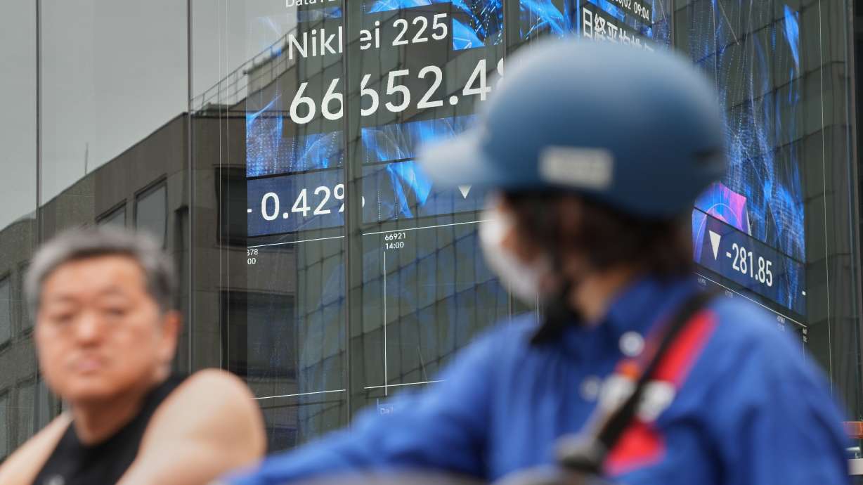 People stop in front of an electronic stock board showing Japan's Nikkei index at a securities firm Tuesday, in Tokyo.
