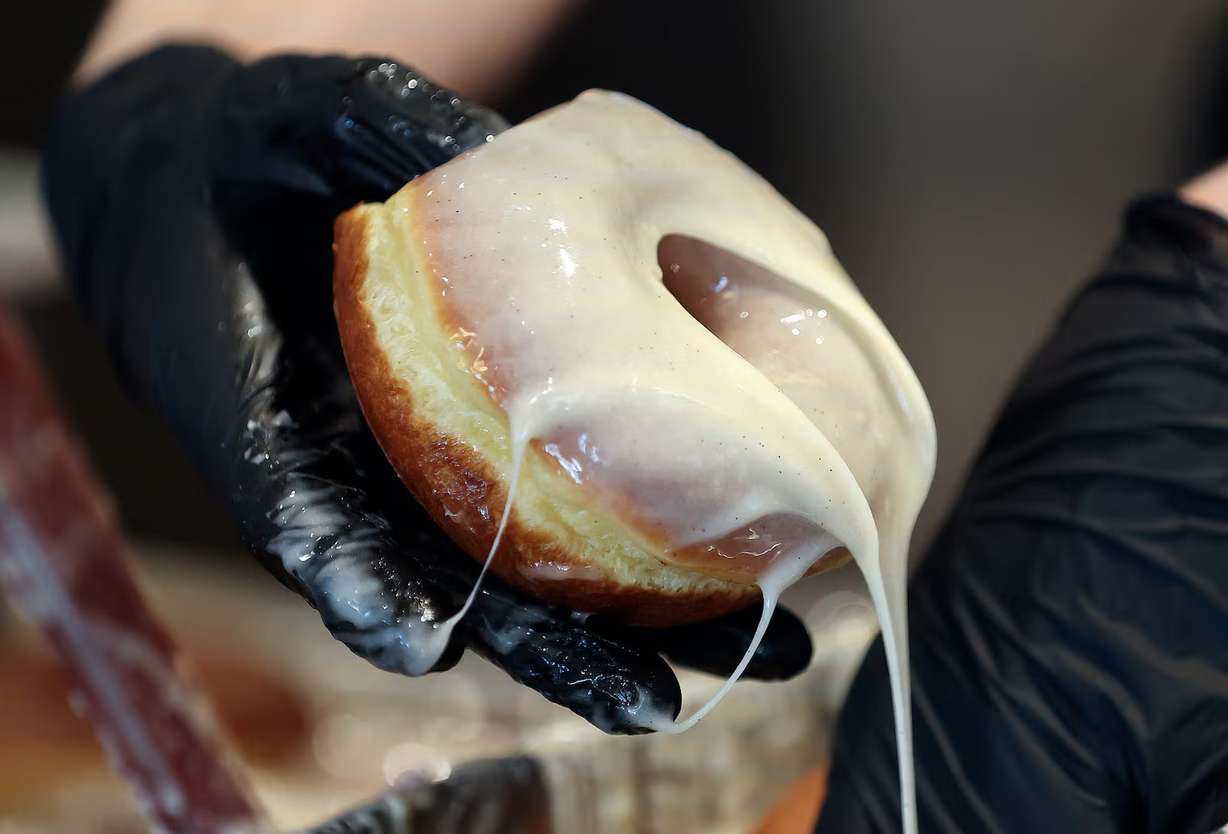 An employee glazes a doughnut at Sidecar Doughnuts in Salt Lake City on Thursday. The California-based shop is making rewards earners winners on National Doughnut Day on Friday.