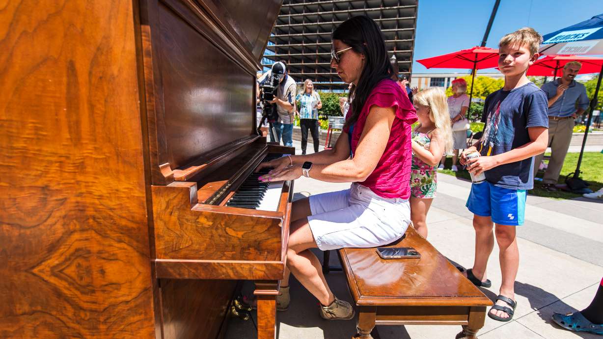 People line up to play a 9-foot-tall, 13-foot-wide piano, the latest version of "Key Changes," in the plaza outside of Abravanel Hall in Salt Lake City on Friday. The playable art piece will remain in the plaza for the summer.