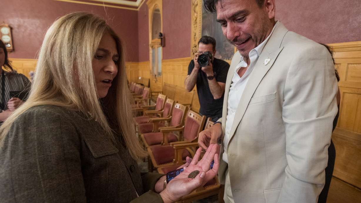 Jennifer Napier-Pearce, left, and Salt Lake City Council Chairman Alejandro Puy, right, holding the coin used to determine the replacement for a vacant Salt Lake City Council seat. Napier-Pearce won the election, keeping the seat through early 2028.