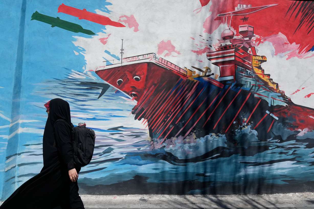 A woman walks past a mural depicting a U.S. aircraft carrier under missile attack in downtown Tehran, Iran, Monday. Both Iran and the U.S. launched airstrikes on the other on Tuesday and Wednesday after President Donald Trump accused Iran of downing an Army helicopter.