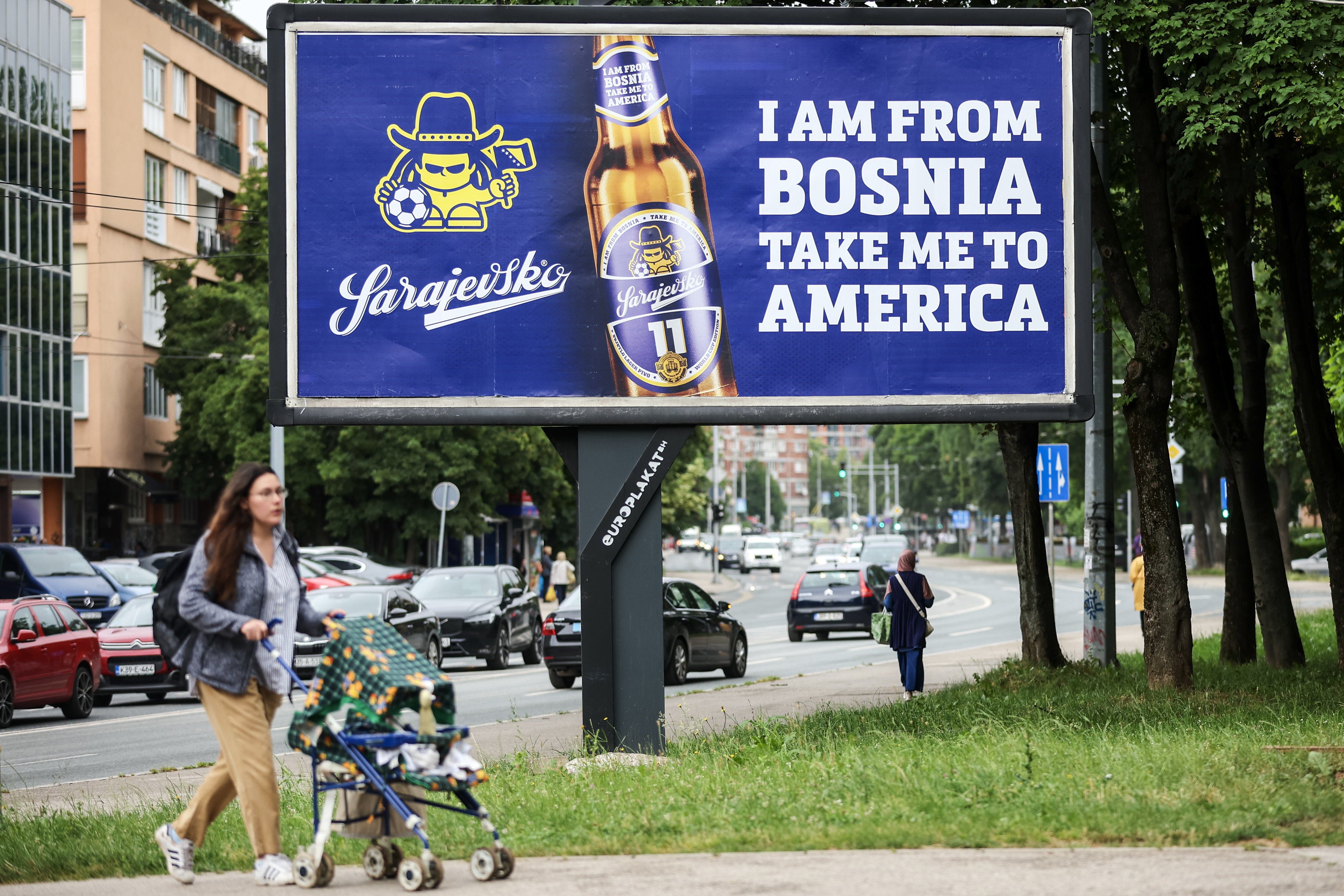 A woman walks past a billboard displaying lyrics from the Dubioza kolektiv song "I Am From Bosnia, Take Me to America" in Sarajevo, Bosnia, Thursday, June 11, 2026.
