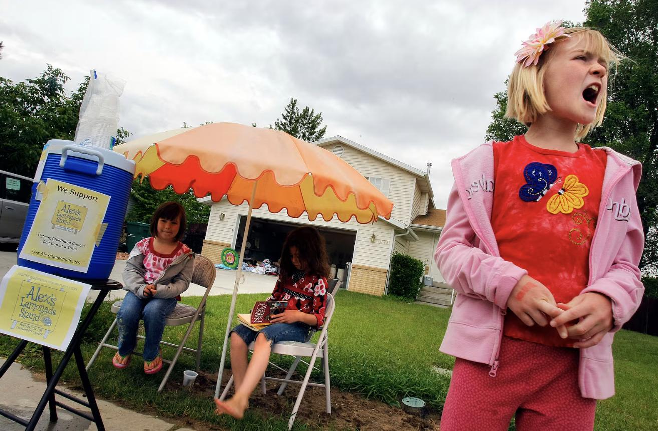 Bailey Foster, right, calls out to cars and passersby trying to sell hot chocolate and lemonade. She is joined by her cousin Chloe Vasko, left, and neighbor Sophia Finlinson, center, on June 12, 2010.