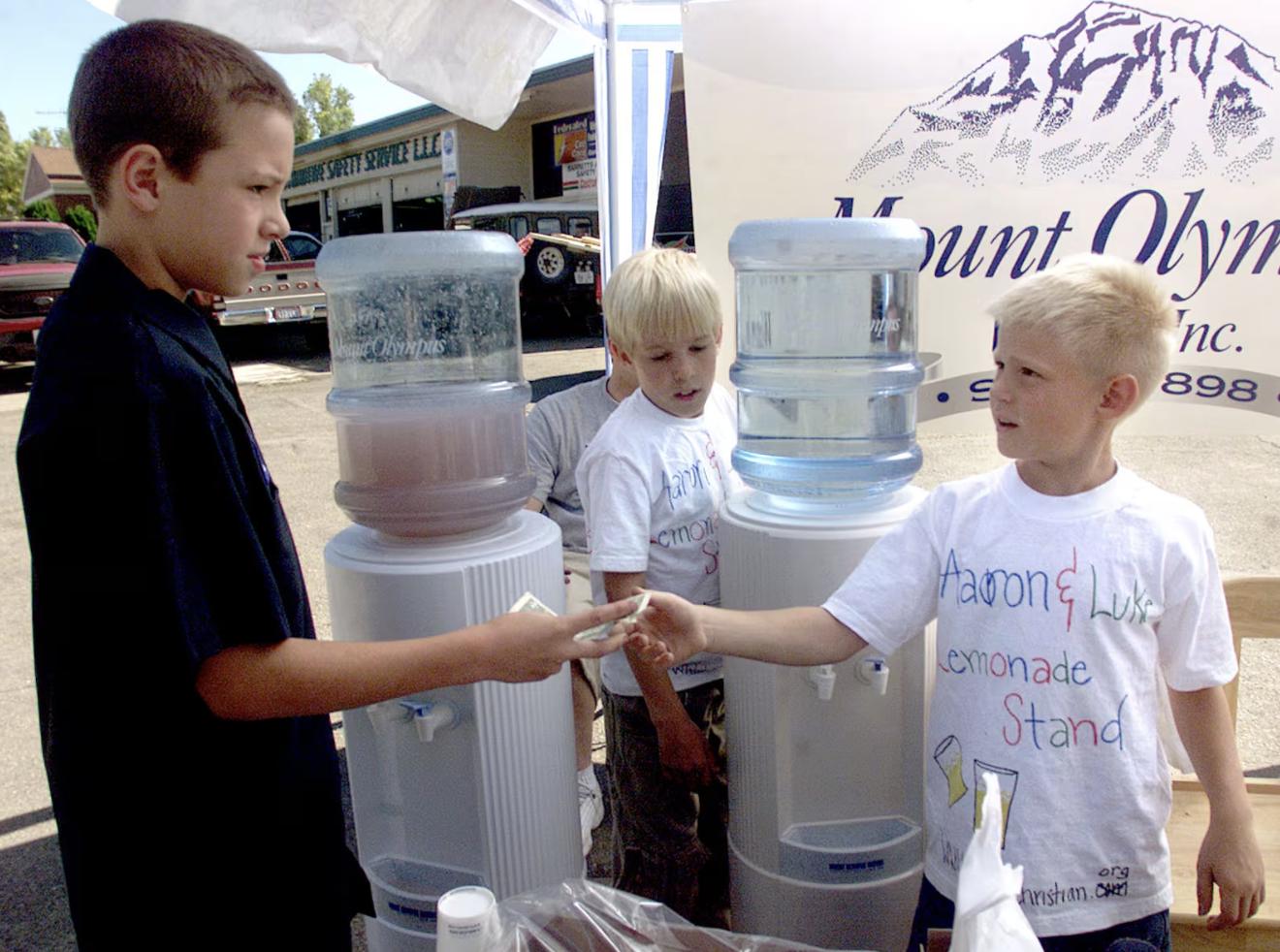 Taylor Stassi (L) buys a glass of lemonade from Aaron (center) and Luke (R) Ahonen who are donating the funds to help thier cousin Hannah pay for medical bills incured by her cancer.
