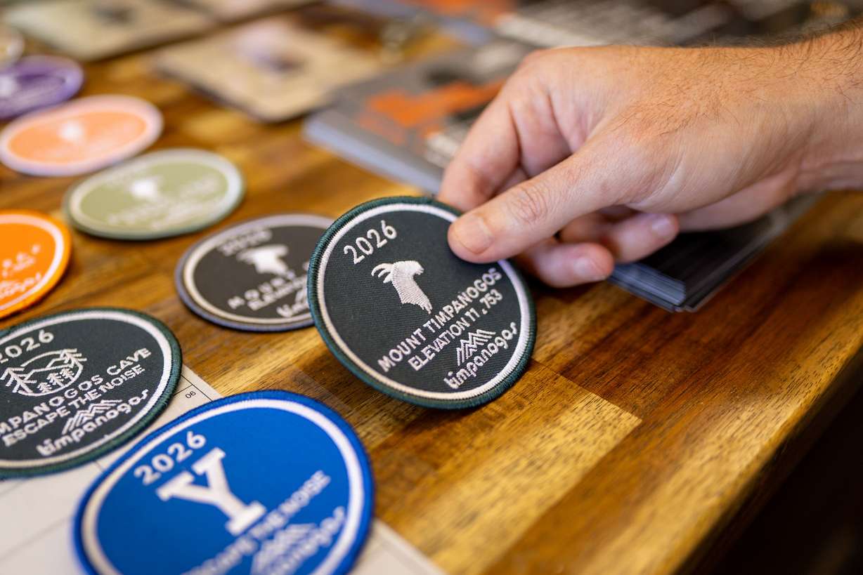 Joe Vogel, owner of Timpanogos Hiking Co., holds a badge that people who have completed the hike on the 2026 Timpanogos Hiking Challenge can pick up at his store Timpanogos Hiking Co. in Provo on June 12.