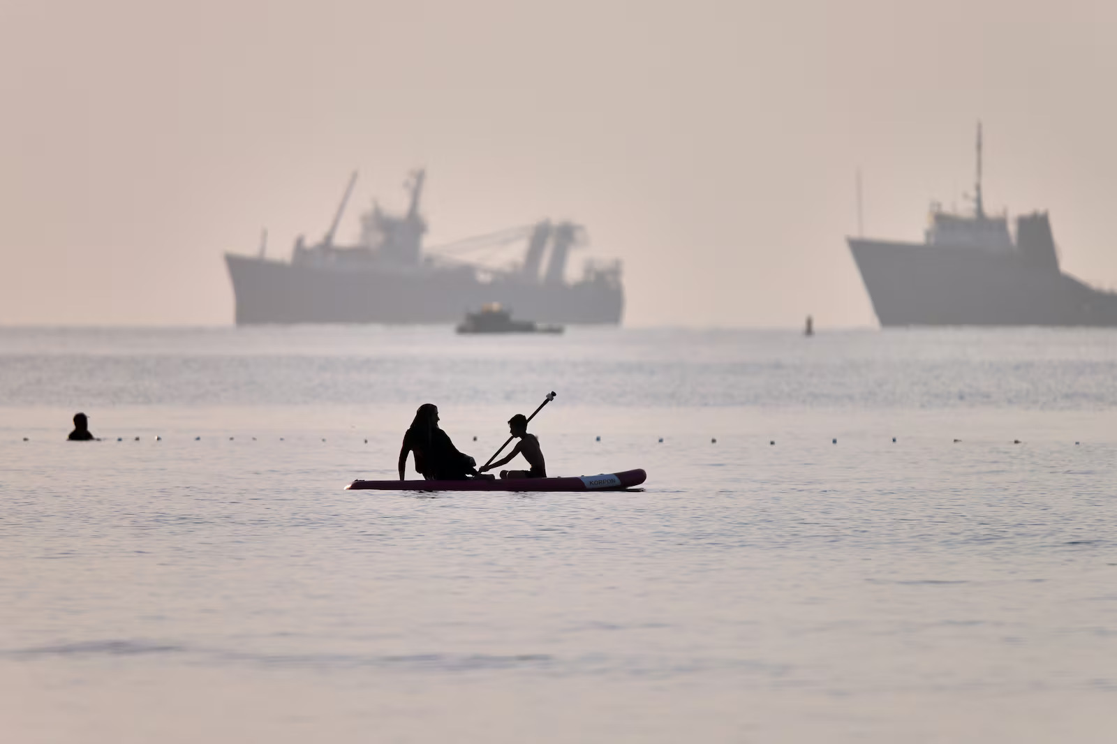 People ride a paddleboard as cargo and service vessels are anchored in the Strait of Hormuz off Bandar Abbas, Iran, June 1. A new deal to end the war in Iran includes the opening of the strait.