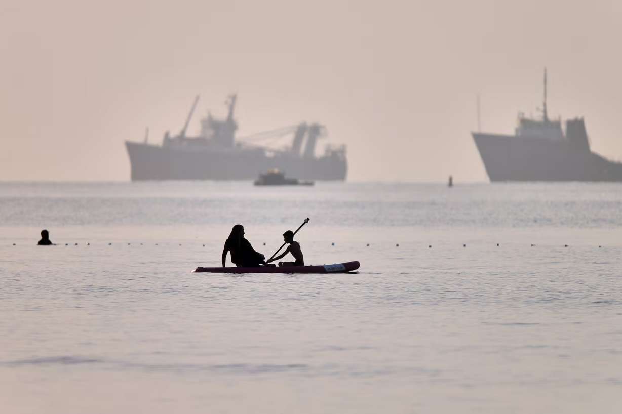 People ride a paddleboard as cargo and service vessels are anchored in the Strait of Hormuz off Bandar Abbas, Iran, June 1. A new deal to end the war in Iran includes the opening of the strait.