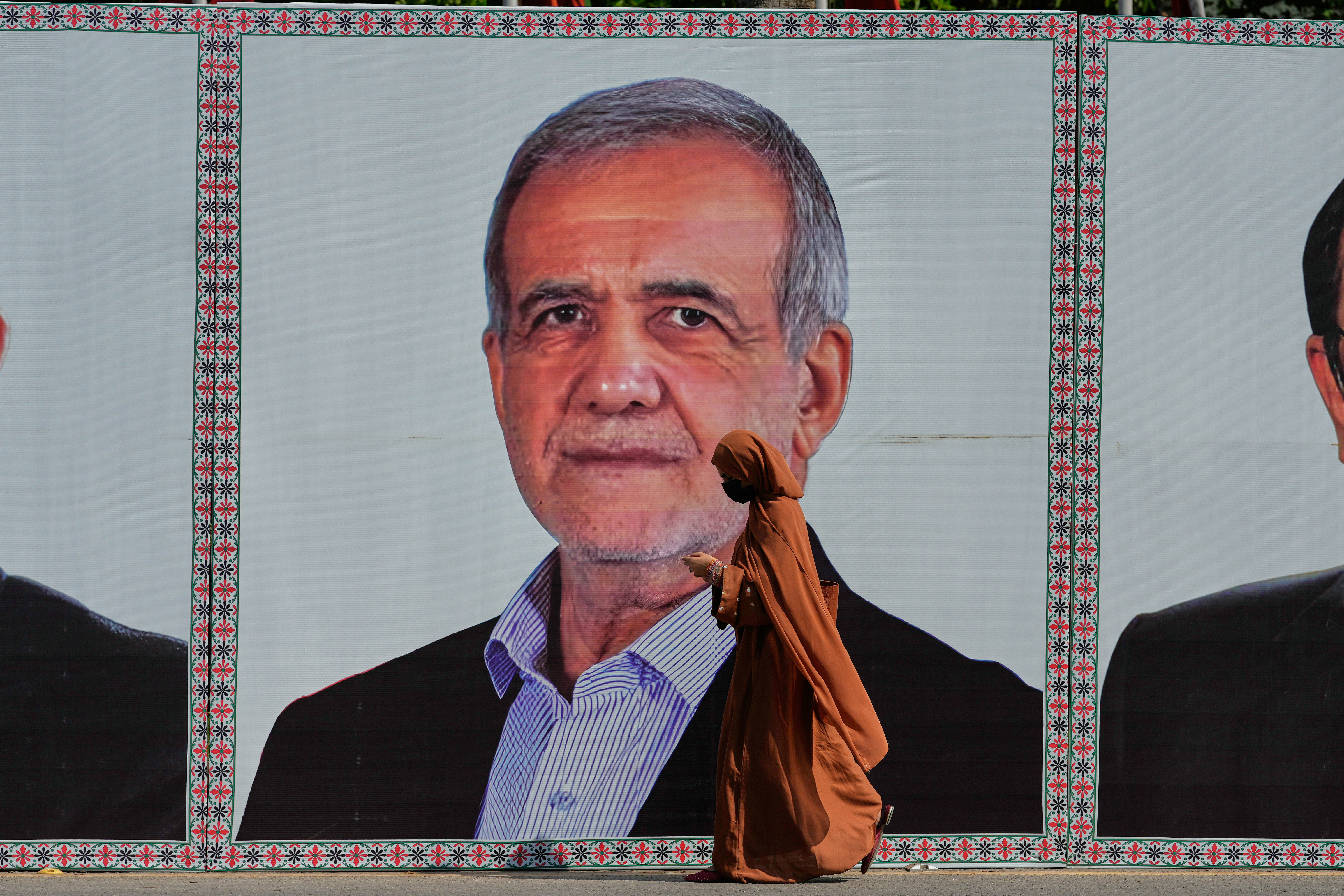 A woman walks past a welcoming billboard featuring Iranian President Masoud Pezeshkian along a roadside in Islamabad, Pakistan, Tuesday. Pezeshkian was in Pakistan for more talks after high-level talks in Switzerland between the U.S. and Iran on Monday.