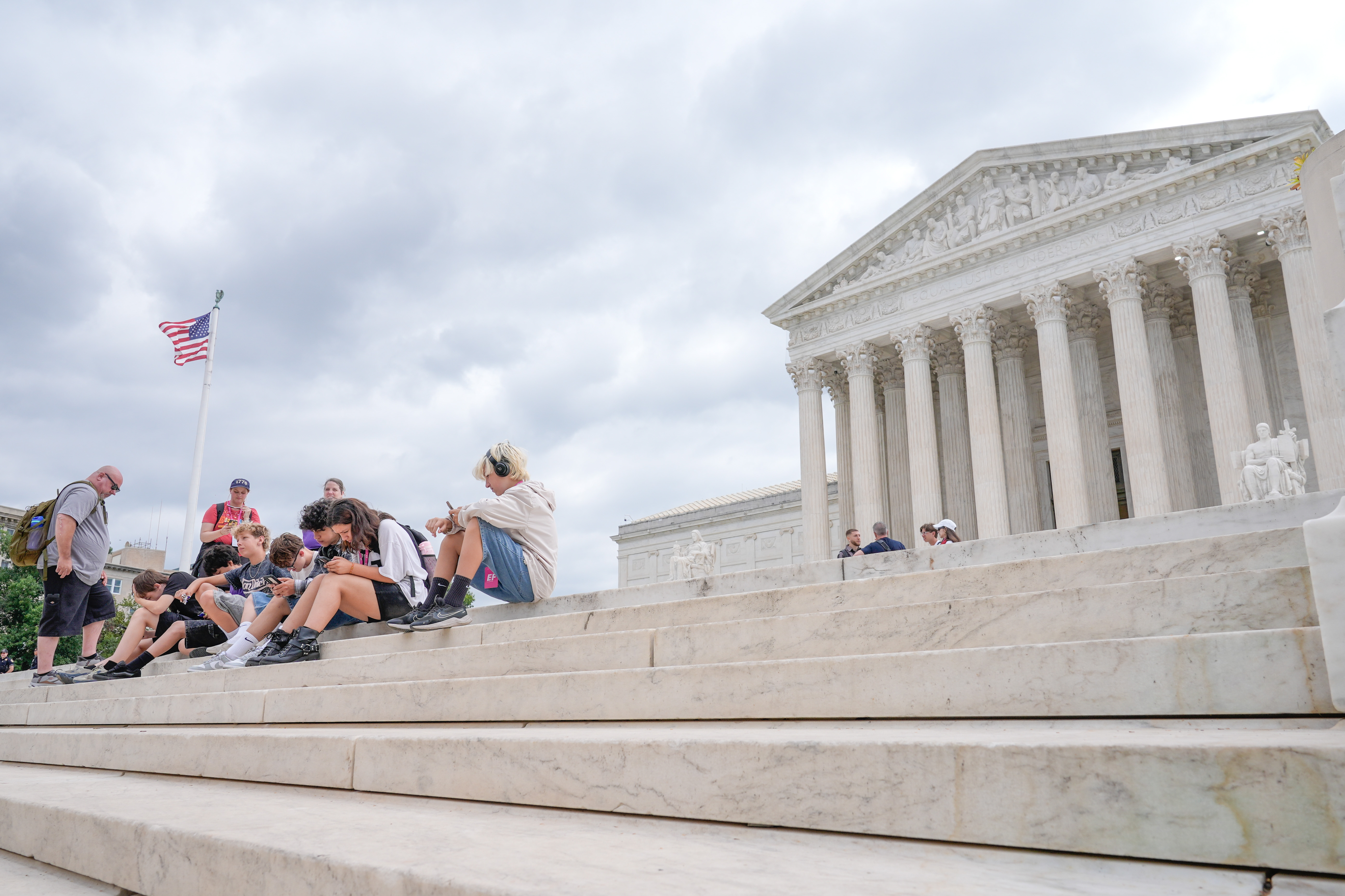 Visitors sit on the steps of the U.S. Supreme Court on Monday, June 8, in Washington.