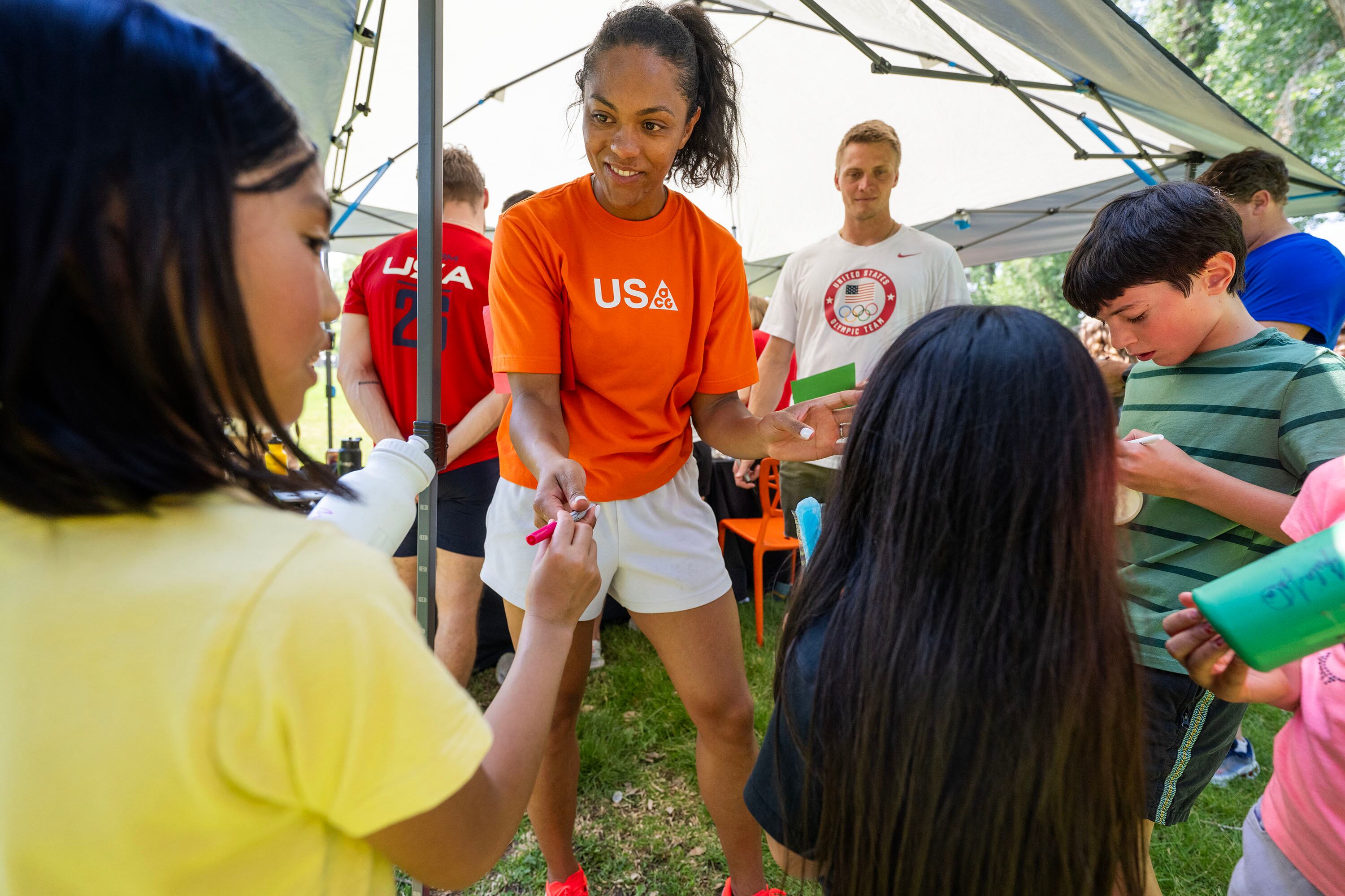 Kaysha Love, bobsled, Hunter Powell, bobsled, and David Blair, para track and field, sign autographs for Eevie, Camila, Jimmy and others as Olympic and Paralympic athletes from the 2026 Milan Cortina Winter Games celebrate global Olympic Day with a morning of workouts with kids at Salt Lake City’s YouthCity program at Liberty Park in Salt Lake City on Tuesday.