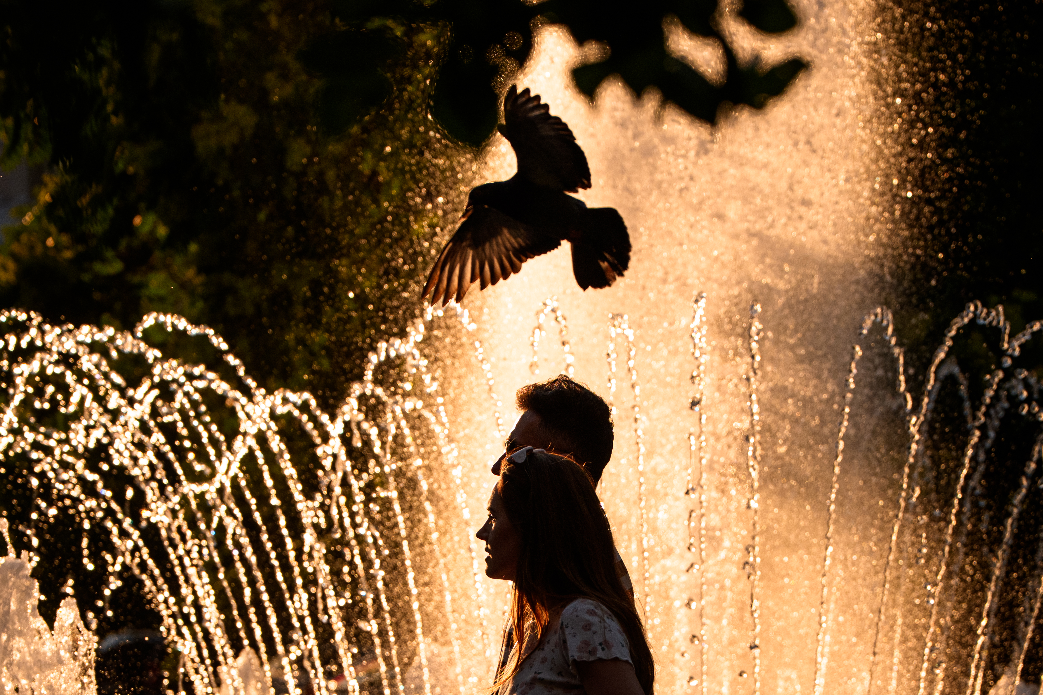 A couple walks by a public fountain on a torrid day, as the National Weather forecaster issued an extreme heat code red warning for parts of the country, in the coming days in Bucharest, Romania, Saturday.