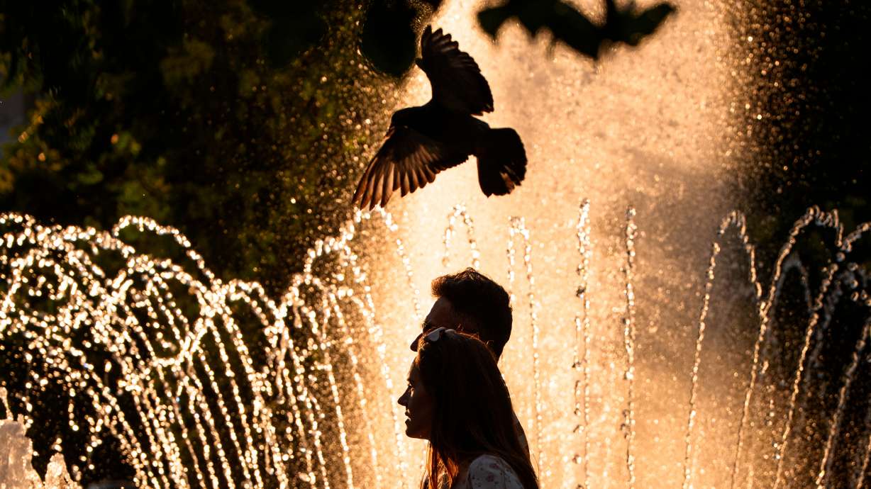 A couple walks by a public fountain on a torrid day, as the National Weather forecaster issued an extreme heat code red warning for parts of the country, in the coming days in Bucharest, Romania, Saturday.