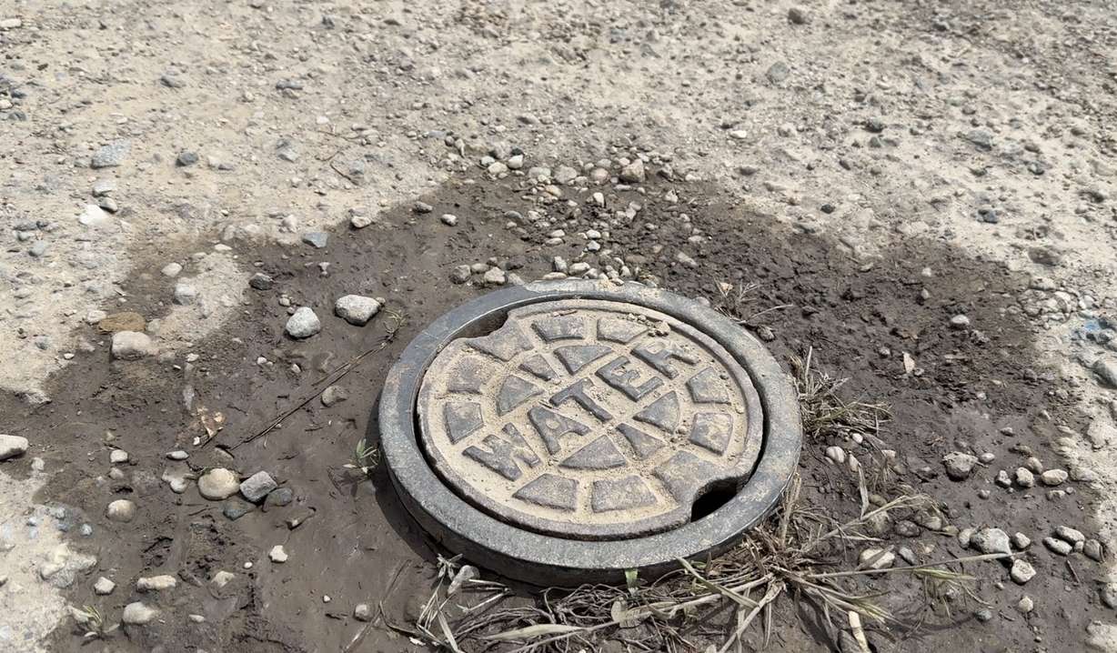 A water cover sits in mud and gravel in an Ogden neighborhood where residents learned they may be responsible for private pipes once tied to an HOA.