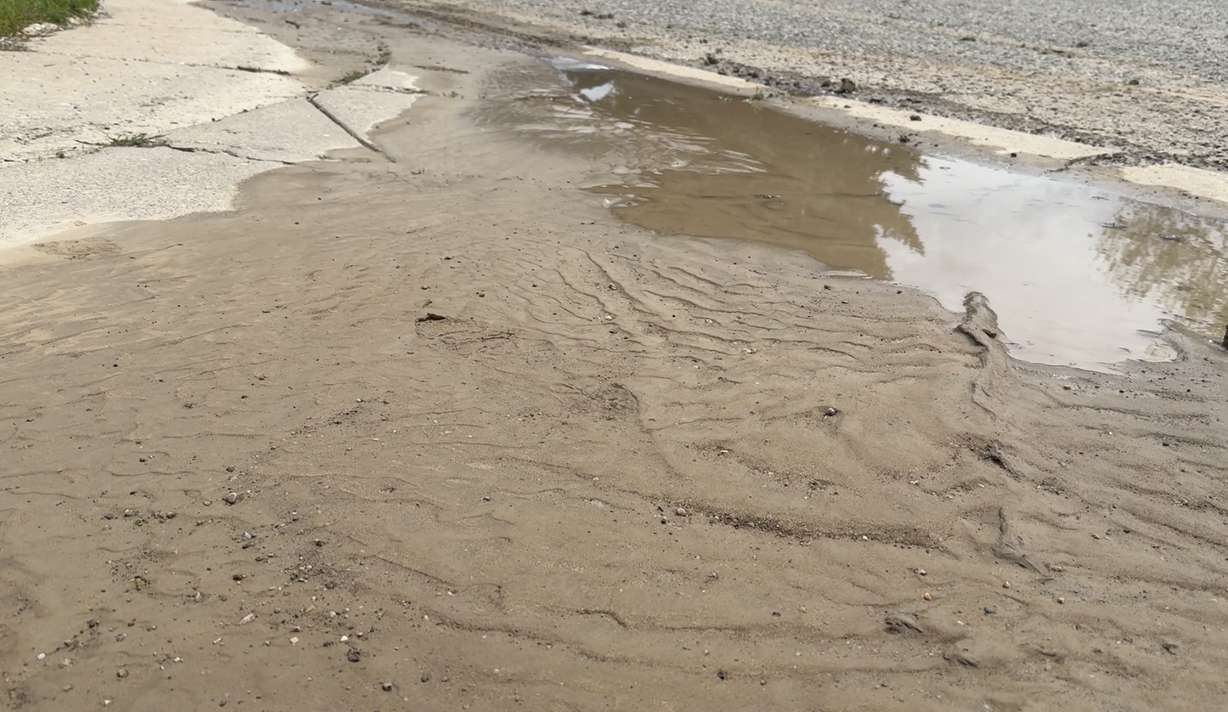 Muddy water pools along a street in an Ogden neighborhood after a water main break raised questions about who pays when an HOA stops operating.