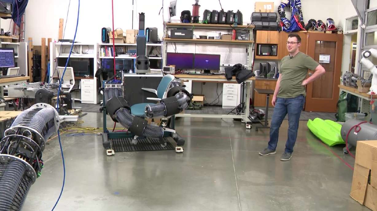 BYU student Curtis Johnson standing next to his robot as it carries an object.