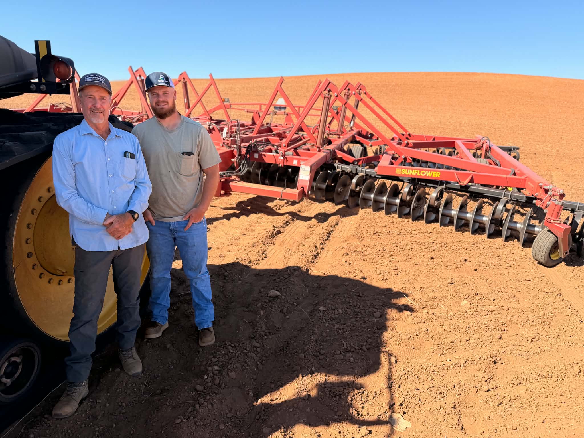 Scott Johnson and his son, Zach Johnson, stands next to a disc harrow on Tuesday.
