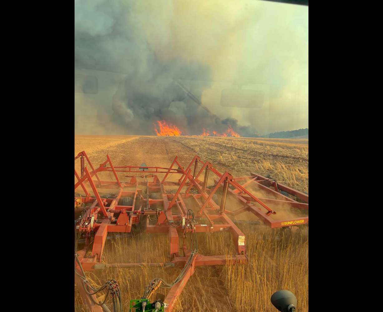 Zach Johnson inside his tractor, pulling a disc harrow through his wheat field as the Horse Head Fire grows on Saturday.