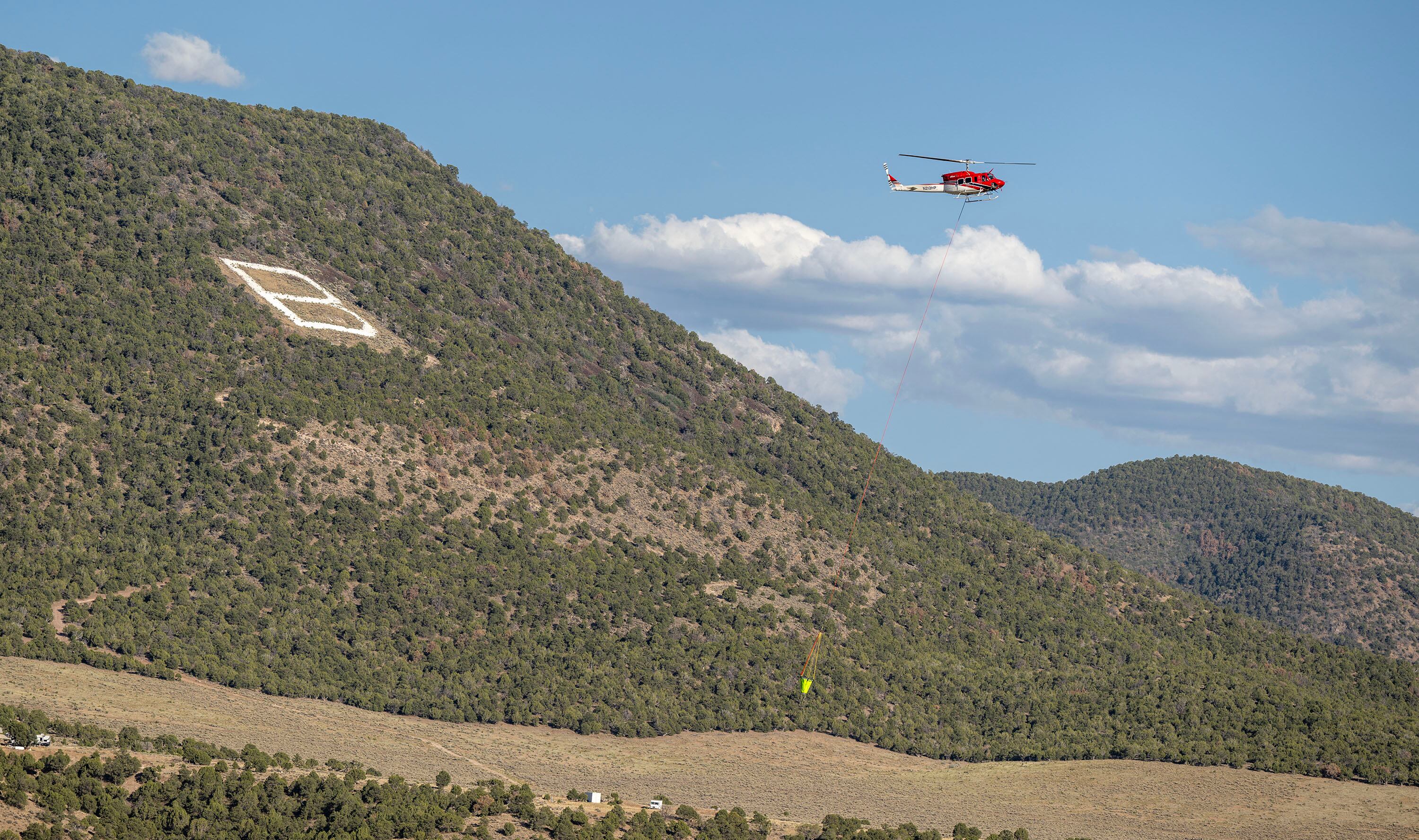 A helicopter flies over the “B” on the hillside as it heads back for more water to drop on the Cottonwood Fire that continues to burn east of the town of Beaver on Tuesday. The fire is the largest nationwide and in the state.