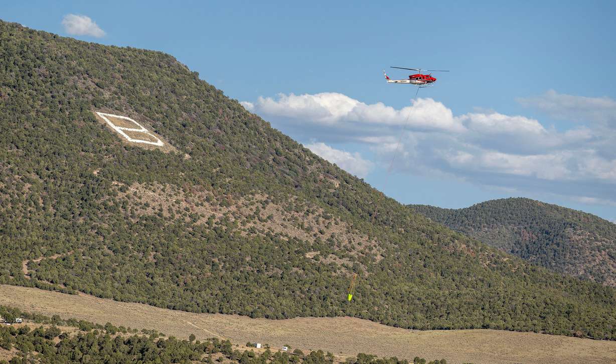 A helicopter flies over the “B” on the hillside as it heads back for more water to drop on the Cottonwood Fire that continues to burn east of the town of Beaver on Tuesday. The fire is the largest nationwide and in the state.